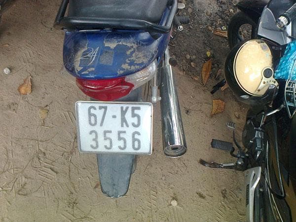 The back of a dusty blue scooter parked on sand, with a white plate reading 67-K5 3556